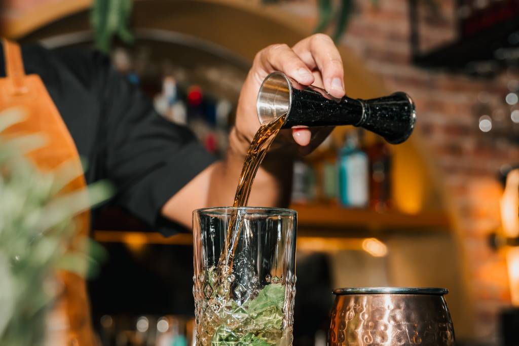 A close-up photo of a bartender’s hand pouring a shot into a glass.