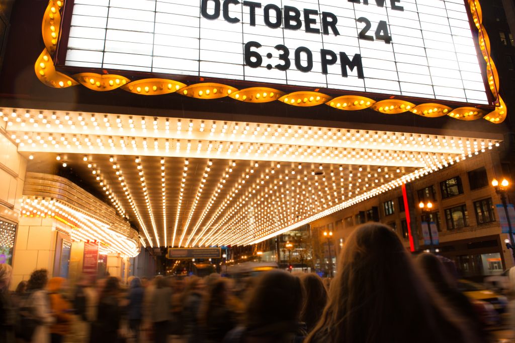 A crowd of people under a glowing marquee sign.
