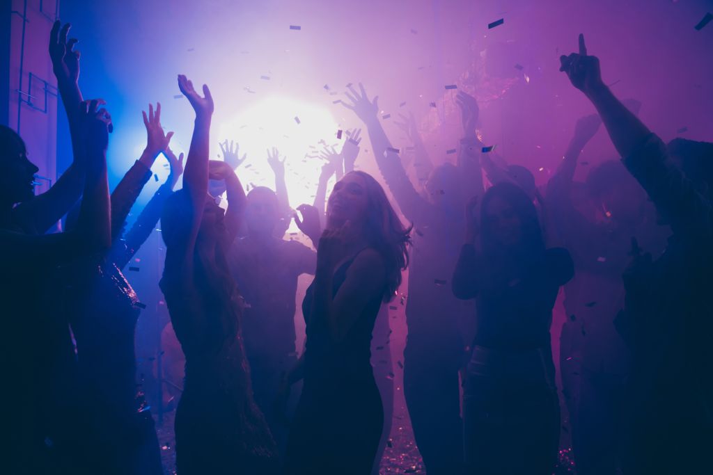 Nightclub clients dancing in smoke, colored lights, and confetti.